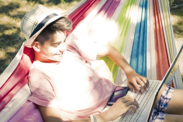 Adolescent qui fait ses travaux scolaires sur son portable dans un hamac au soleil